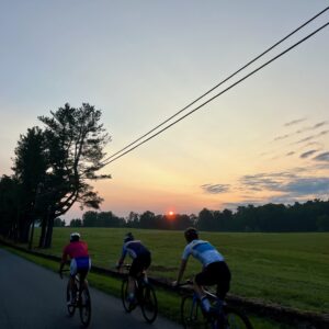 Three people riding bicycles on Ortman Road at sunrise